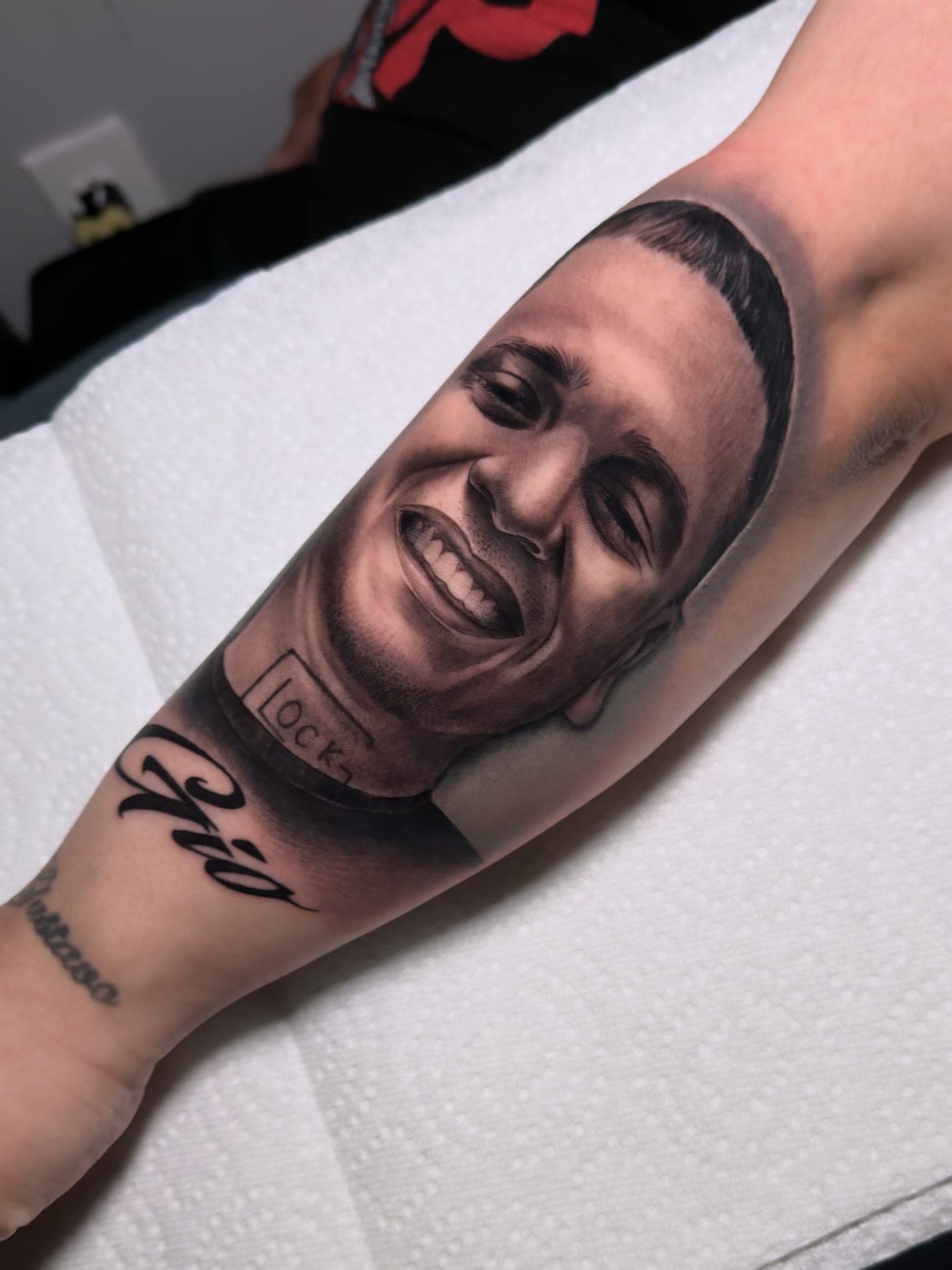 Black and grey realism portrait of a smiling young man on forearm