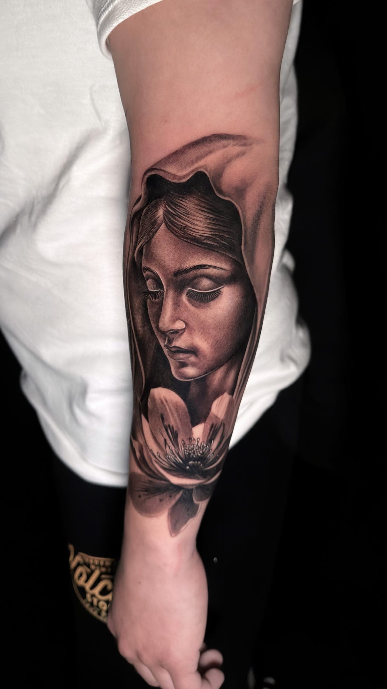 Black and grey Virgin Mary forearm tattoo with flower